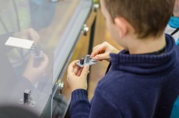 Ein Kind von hinten, welches ein technisches Bauteil in den Händen hält und begutachtet