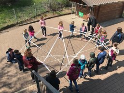 Kinder, die stehend einen Kreis bilden und ein Netz aus Seilen zwischen sich spannen