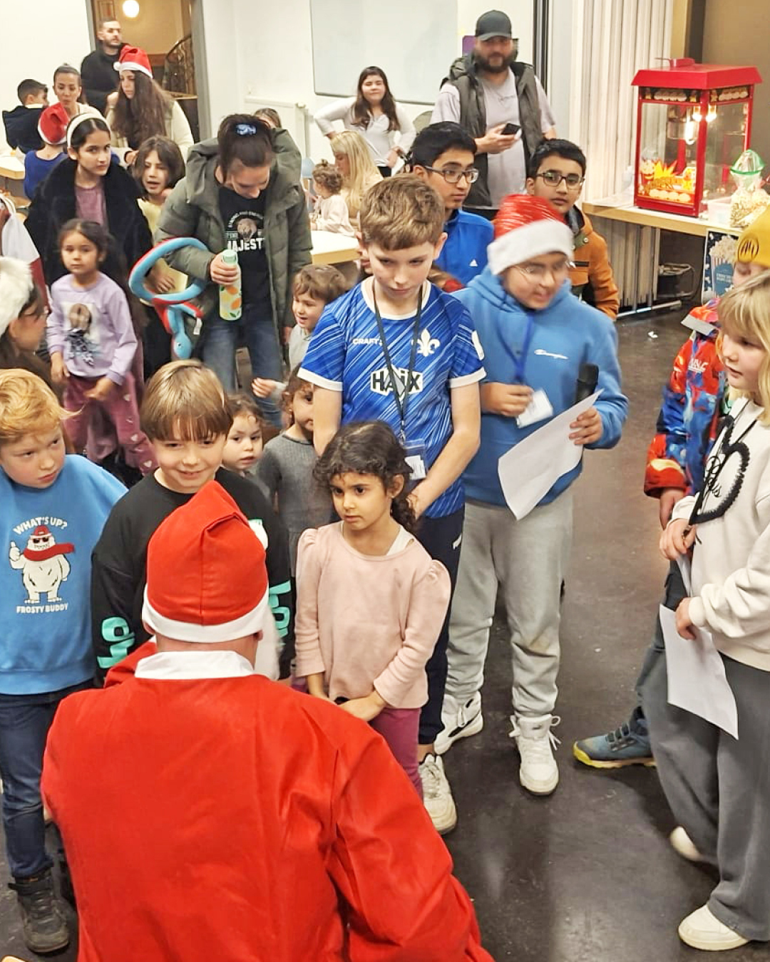 Im Foto ist der Weihnachtsmann von hinten zu sehen, vor ihm stehen Kinder, die auf ihr Nikolausgeschenk warten