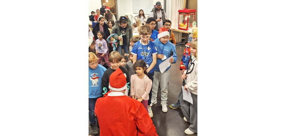 Im Foto ist der Weihnachtsmann von hinten zu sehen, vor ihm stehen Kinder, die auf ihr Nikolausgeschenk warten