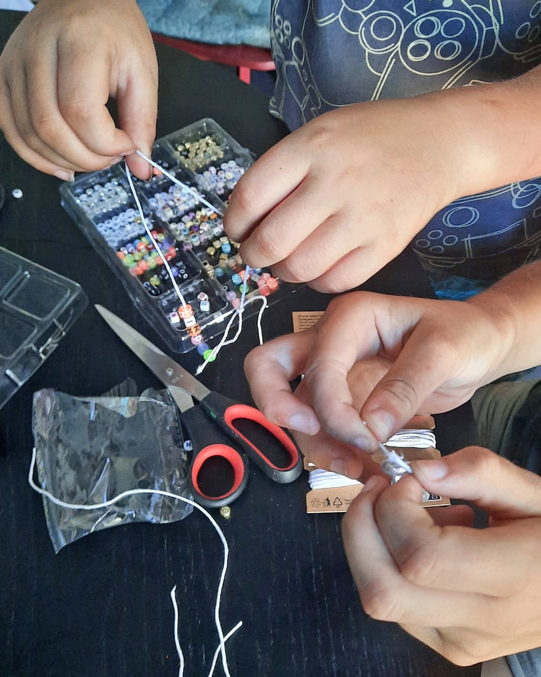Café kreativ – freitags im ZIMMnER Auf dem Foto sieht man Kinderhände beim Gestalten von Perlenarmbändern