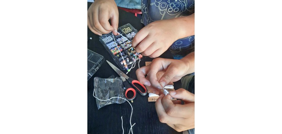 Auf dem Foto sieht man Kinderhände beim Gestalten von Perlenarmbändern