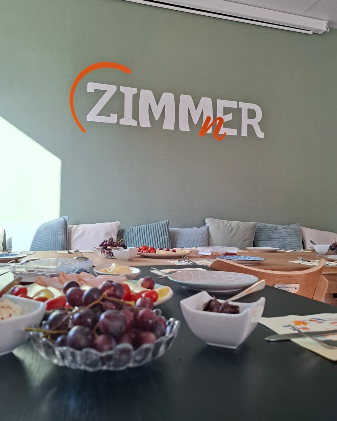 FrühstücksKlatsch Gedeckter Frühstückstisch, im Hintergrund die grüne Wand des ZIMMnERs mit Logo