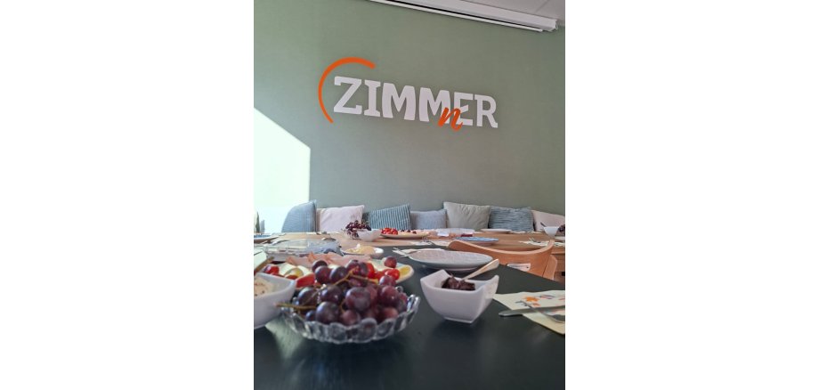 FrühstücksKlatsch Gedeckter Frühstückstisch, im Hintergrund die grüne Wand des ZIMMnERs mit Logo